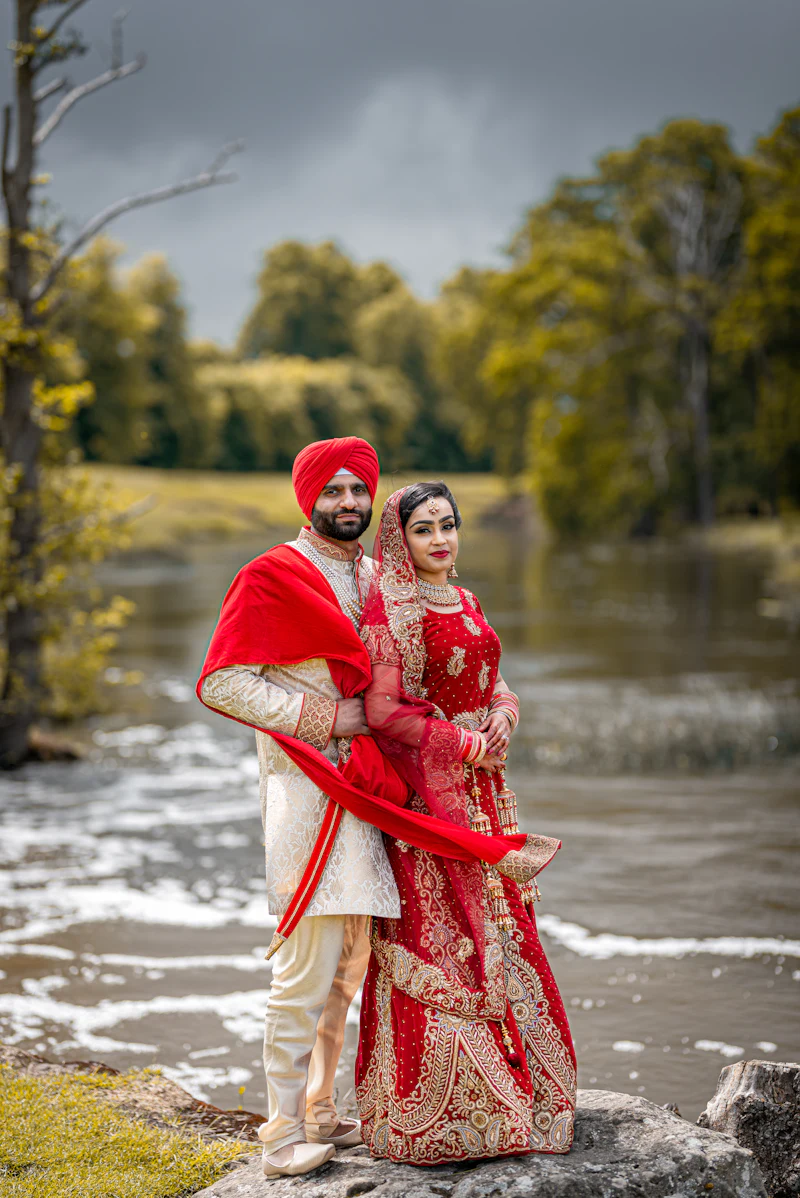 A couple in Punjabi wedding attire standing by a river